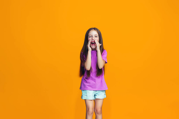 Isolated on orange young casual teen girl shouting at studio - 写真・画像