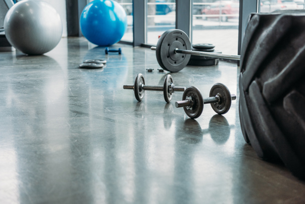 barbell, dumbbells, fitness balls and training tire on floor at gym - Photo, Image