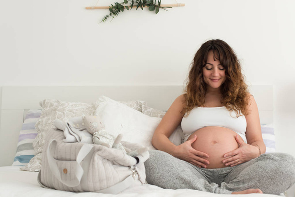 Happy pregnant woman sitting and touching her belly at home - Valokuva, kuva