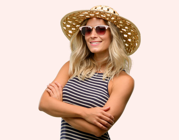 Fiatal nő segítségével napszemüveg viselése nyári kalap keresztezett karokkal, magabiztos és elégedett egy nagy természetes mosoly, nevetés - Fotó, kép