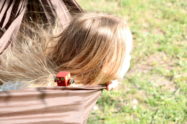 beautiful little girl with blond hair resting in a hammock in summer sunny day - Zdjęcie, obraz
