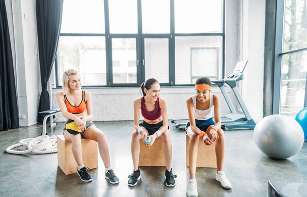 three happy multicultural resting on wooden boxes at gym  - Photo, Image