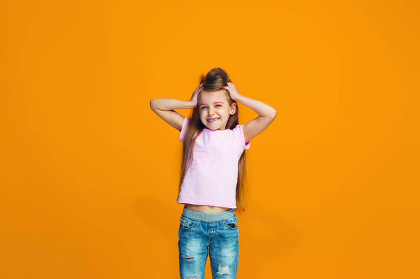 The happy teen girl standing and smiling against orange background. - Фото, изображение