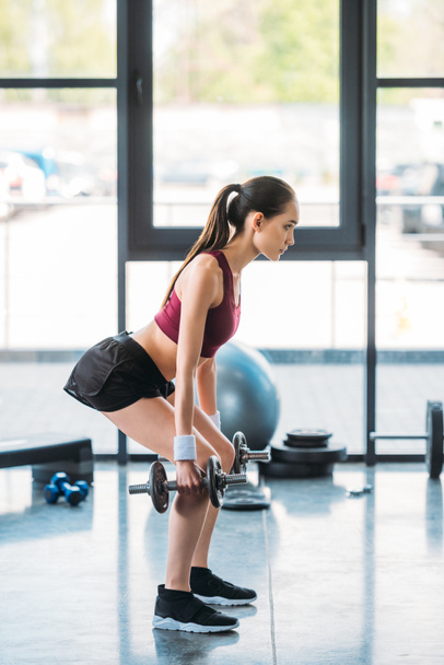 vista lateral de la deportista asiática haciendo ejercicio con pesas en el gimnasio
 - Foto, Imagen