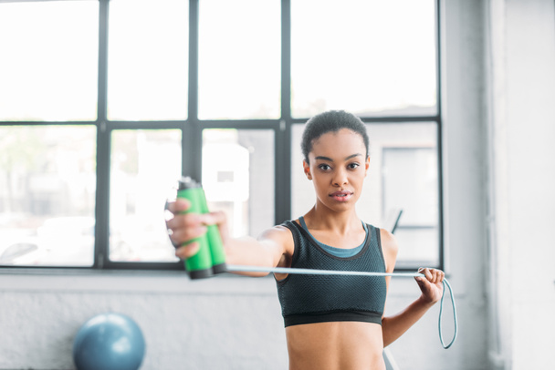 portrait of young african american sportswoman with jumping rope at gym - Фото, изображение