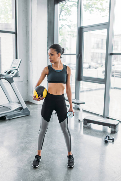 african american sportswoman with ball and sportive water bottle at gym - Foto, Imagem