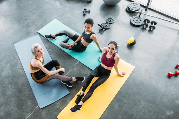 Blick aus der Vogelperspektive auf junge multikulturelle Sportlerinnen, die nach dem Training im Fitnessstudio auf Matten ruhen - Foto, Bild