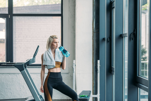 young sportswoman with towel drinking water from sportive water bottle after workout at gym - Foto, Bild