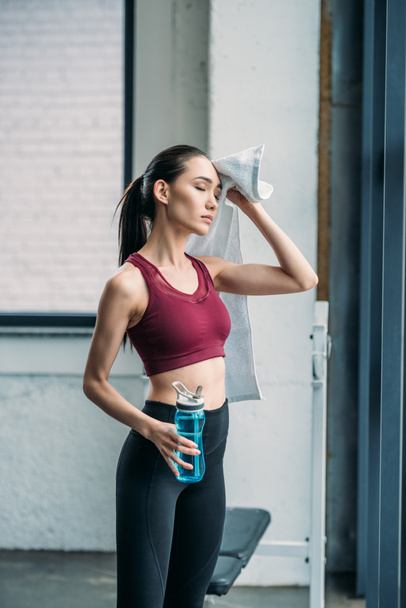 tired asian sportswoman with towel and water bottle after workout at gym - Fotografie, Obrázek