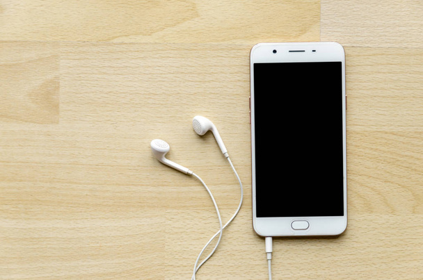 Blank screen smartphone with earphone on wooden table Top corner - Photo, Image