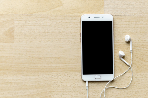 Smartphone tela em branco com fone de ouvido na mesa de madeira canto superior
 - Foto, Imagem