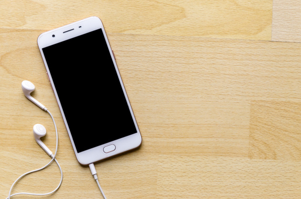 Smartphone à écran blanc avec écouteur sur table en bois coin supérieur ont stylo adaptateur thé sd
 - Photo, image