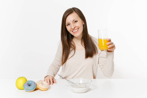 Nuori nainen istuu pöydän ääressä aamiainen muroja ja maitoa, appelsiinimehua lasissa, munkkeja eristetty valkoisella taustalla. Oikea ravitsemus, herkullinen maukas ruoka, terveellinen elämäntapa. Alue, jolla kopioidaan tilaa
 - Valokuva, kuva