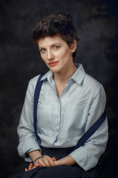 Studio portrait of beautiful pensive middle age brunette Caucasian woman looking in camera. Girl female with short boyish  hair style wearing shirt and suspenders. - Valokuva, kuva