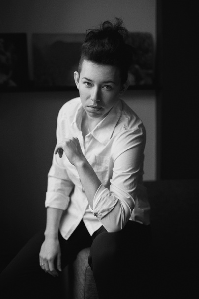 Closeup zwart-wit portret van mooie sexy edgy jonge Kaukasische vrouw. Europese vrouw met donker haar zittend op banklaag binnenshuis. Androgeen jongensachtige gestileerde schieten. Film lawaai graan imitatie - Foto, afbeelding