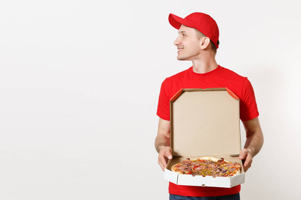Entrega hombre sonriente en uniforme rojo aislado sobre fondo blanco. Pizzaman masculino en gorra, camiseta que trabaja como mensajero o distribuidor sosteniendo pizza italiana en caja plana de cartón. Copiar espacio para publicidad
 - Foto, imagen