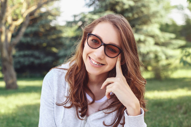 Gros plan portrait de belle jeune femme souriante caucasienne européenne aux cheveux roux portant des lunettes de soleil. Jeune fille adolescente avec bretelles
  - Photo, image