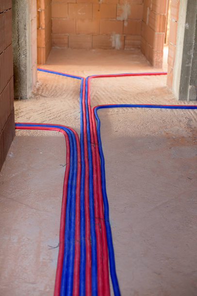 Dos tubos de colores, azul y rojo, en el suelo - instalación de calefacción
 - Foto, imagen