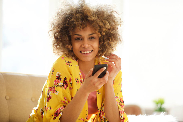 Porträt einer attraktiven jungen Frau, die zu Hause mit dem Handy sitzt - Foto, Bild