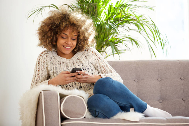 Porträt einer jungen Afrikanerin, die sich zu Hause entspannt und ihr Handy benutzt - Foto, Bild