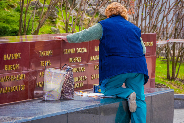 MOSCOW, RUSSIA- APRIL, 29, 2018: Outdoor view of eldery woman wearing blue jacket in the park painting with golden color the letters of outdoor structure on red square in Moscow - Фото, зображення