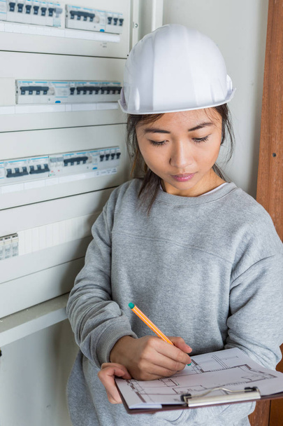 female electrician with clip-board next to fuse box - Foto, afbeelding