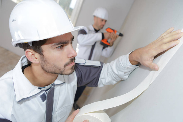 Worker applying masking tape to wall - Foto, Bild