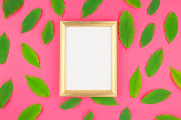 Creative flat lay top view pattern with fresh green leaves on bright pink background with golden frame mock up and copy space in minimal pop art style, template for text - Фото, зображення