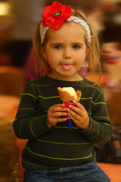 Lähikuva muotokuva hauska lapsi tyttö syö jäätelöä hänen kielensä ulos
 - Valokuva, kuva