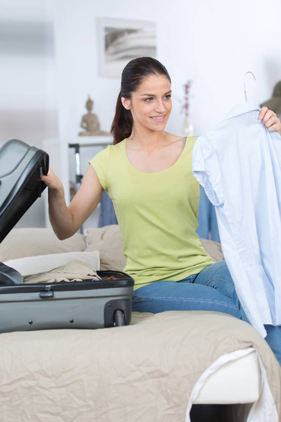 happy female traveler sitting on bed and packing suitcase - 写真・画像