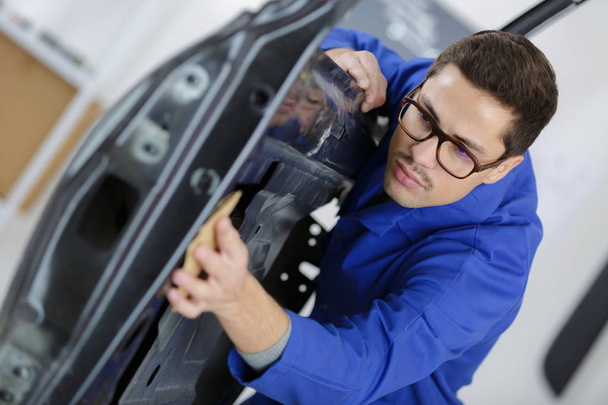 portrait of handsome mechanic in uniform cleaning car door - Fotoğraf, Görsel