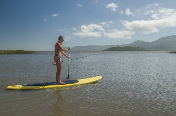 Young woman practicing Stand Up Paddle on lake, yellow board, paddling. Paddleboarding. - Fotó, kép