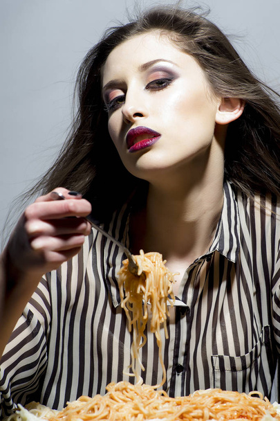 Young beautiful woman eating spaghetti on grey background. - Foto, afbeelding