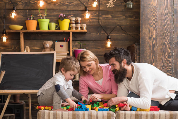 Father, mother and cute son play with constructor bricks. Kid with parents play with plastic blocks, build construction. Caring parents concept. Family on busy face spend time together in playroom. - Valokuva, kuva
