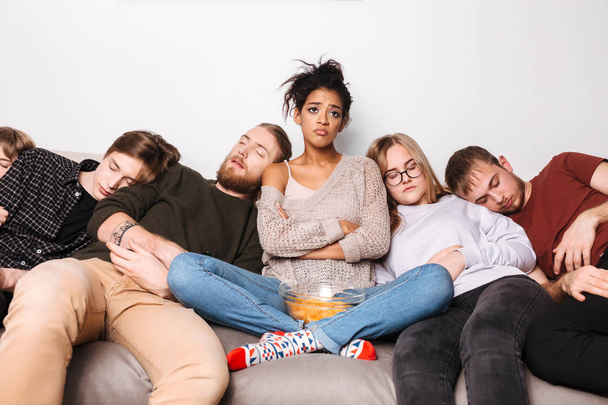 Muotokuva nuori järkyttynyt nainen istuu sohvalla pelimerkkejä ja valitettavasti sivuun, kun hänen ystävänsä nukkuvat lähellä kotona
 - Valokuva, kuva