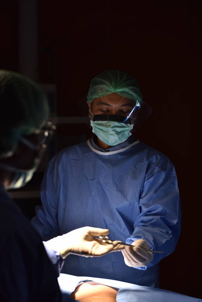 Team chirurg aan het werk in de operatiekamer. Chirurgisch licht in de operatiekamer. Voorbereiding voor het begin van chirurgische ingreep met een snede. De chirurg voert een operatie uit op de patiënt.. - Foto, afbeelding