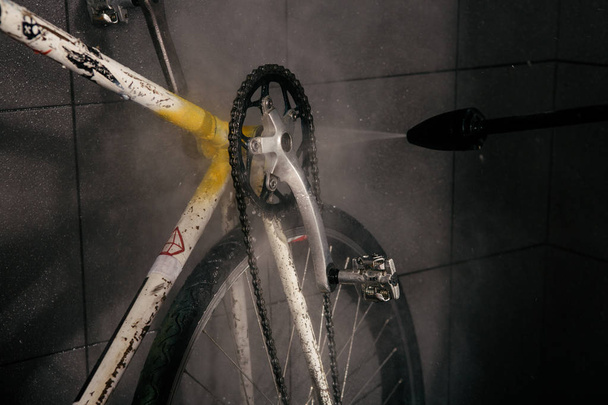 Services professional washing of bicycle in the workshop. Close-up of hand Young Caucasian stylish man doing bicycle cleaning using an automatic electric water pump. Sprays scatter from the pressure. - Photo, Image
