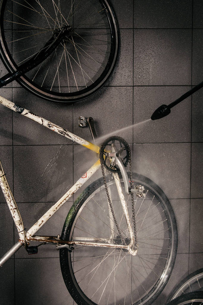 Services professional washing of bicycle in the workshop. Close-up of hand Young Caucasian stylish man doing bicycle cleaning using an automatic electric water pump. Sprays scatter from the pressure. - Photo, Image