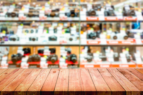 Tavolo vuoto in legno con sfondo sfocato del negozio della macchina fotografica. Per visualizzare o montare i tuoi prodotti
. - Foto, immagini