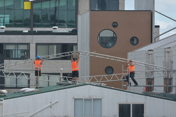Constructores irreconocibles montando un marco de metal en la parte superior de un techo del edificio
. - Foto, Imagen