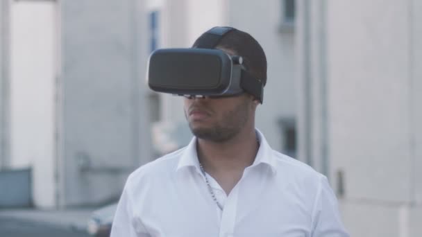 Joven empresario afroamericano en camisa blanca usando casco de realidad virtual en la ciudad. Exterior
. - Metraje, vídeo