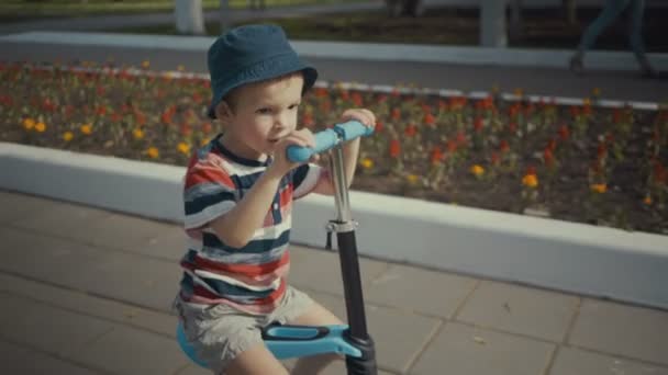 Joyeux petit garçon de deux ans, chevauchant un scooter dans un parc d'été
 - Séquence, vidéo
