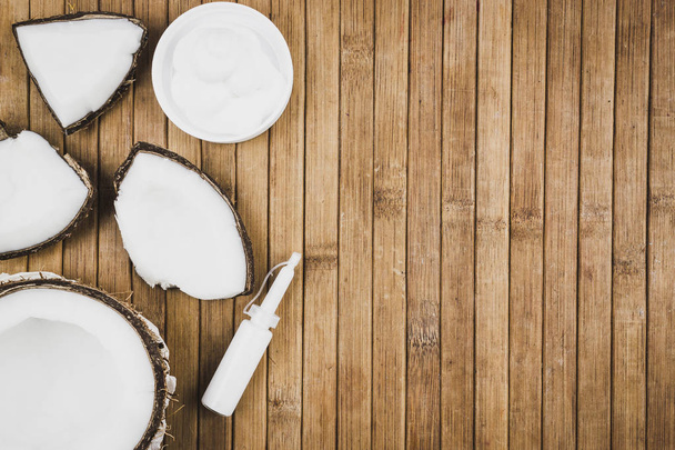 Coconut pieces and cosmetics on a wooden table. Coconut milk cream and butter. Copy space for text - Foto, afbeelding