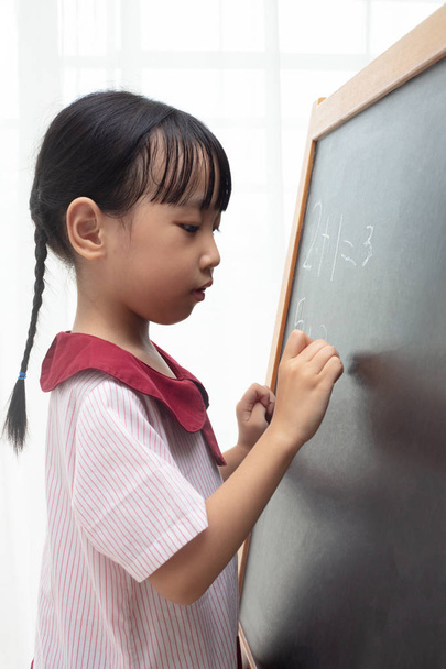 Asian Chinese little girl writing on blackboard in isolated white background - Foto, immagini