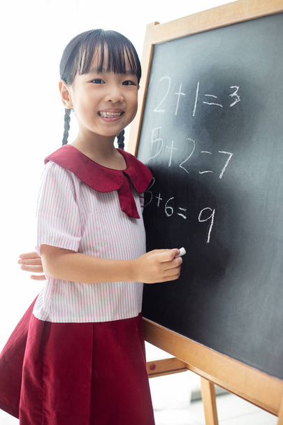 Asian Chinese little girl writing on blackboard in isolated white background - Foto, imagen
