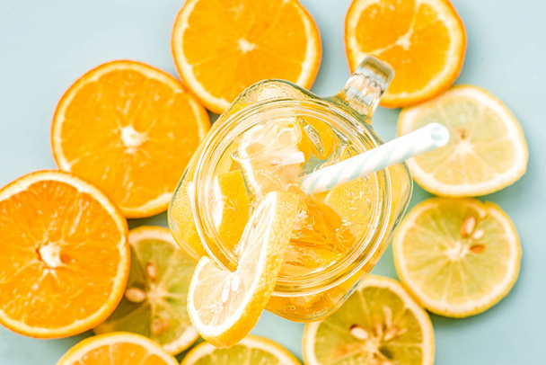 lemonade in a mason jar with a drinking straw decorated with slices of citrus oranges and lemons top view on blue - Photo, Image