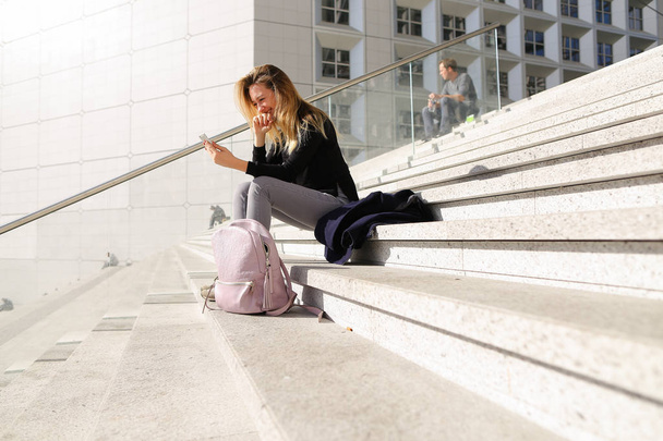 Female person sitting on stairs and using smartphone. - Fotó, kép