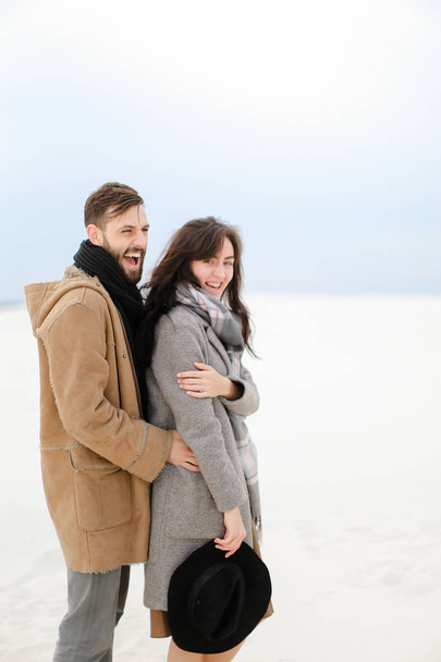Happy young man hugging female person wearing grey coat and scarf, white winter monophonic background. - Fotografie, Obrázek