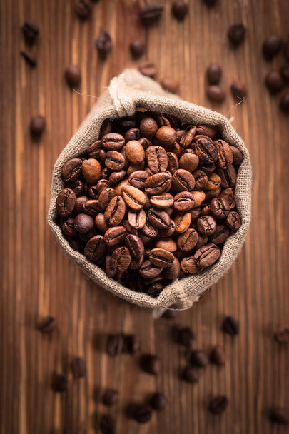 Fresh roasted coffee beans in burlap sack. coffee beans on rustic wooden background - Фото, зображення