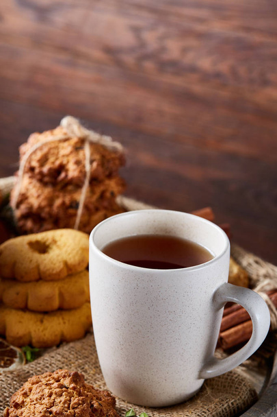 White porcelain cup of hot tea, cookies and spicies on a wooden barrel, selective focus, close-up, vertical. - Foto, afbeelding